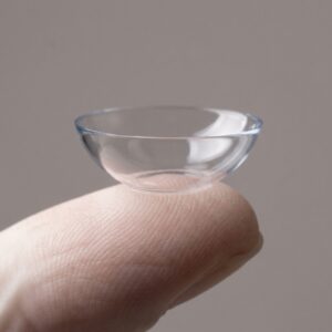 Bowl-shaped scleral lens on a fingertip showing its cup shape